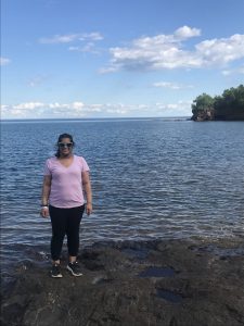 Woman with sunglasses standing near the water's edge on a rocky shore of a lake