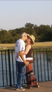 Woman and man embracing for kiss, standing outside near water.
