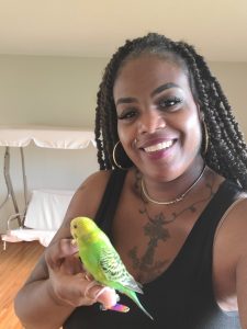Smiling woman indoors with a green and yellow bird perched on her finger.