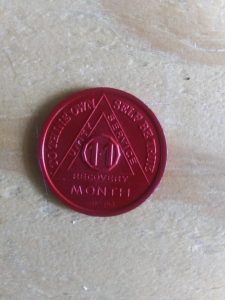 A red recovery coin with words that read: 11 month, unity, service, recovery, to thine own self be true