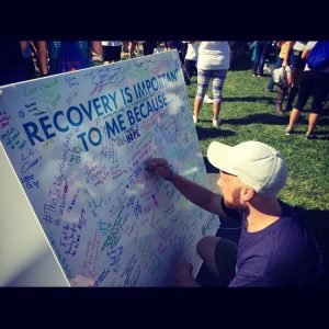 Young man writing on a board, at the Walk for Recovery, why Recovery is Important to him.