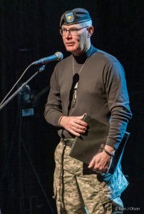 Man in uniform speaking at microphone.