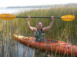 Smiling woman, in kayak on lake, holding paddle above her head.