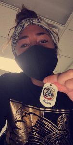 Woman wearing mask, holding necklace tag that reads, Sober Squad 18 Months