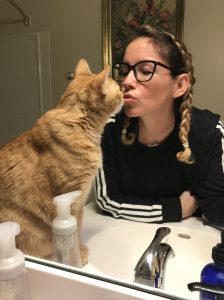 Woman with glasses kissing orange tabby cat.