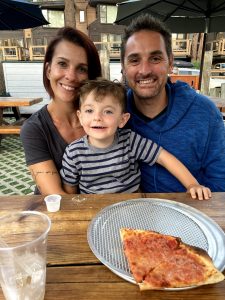 Smiling woman, man, and little boy sitting at a picnic table over pizza lunch